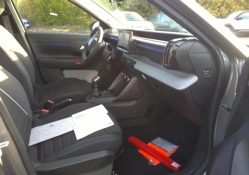 Vue intérieure côté passager avant de la Citroën C3 2025 gris foncé, avec sièges tissu noir et décor bleu sur la planche de bord.