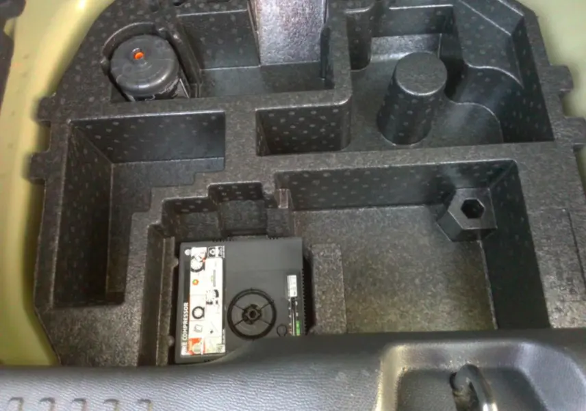 Compartiment de rangement noir sous coffre d'une Citroën C3 2025 gris foncé, vue plongeante sur kit de dépannage.