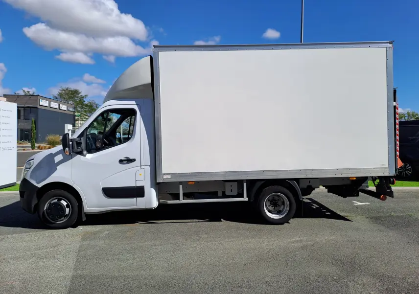Vue de profil côté gauche d’un utilitaire blanc Nissan Interstar Châssis Cabine L3H1 avec caisse fermée sur fond urbain.