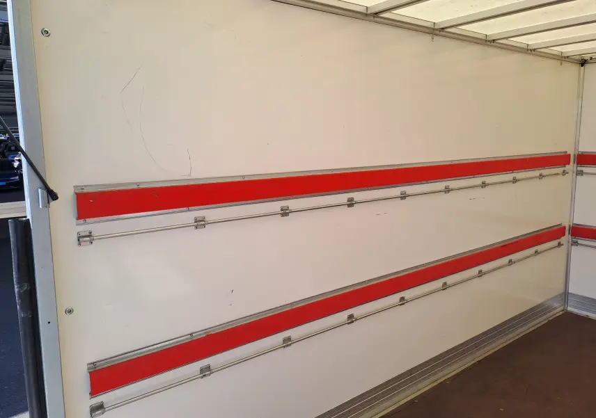 Intérieur du coffre blanc du Nissan Interstar L3H1 2024, avec bandes rouges horizontales et rails métalliques.