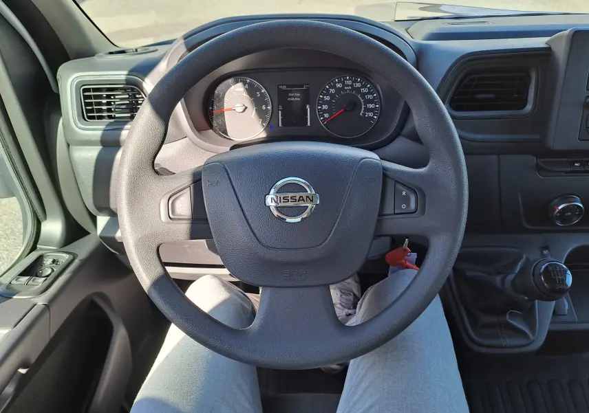 Vue intérieure centrée sur le volant Nissan d’un Interstar blanc 2024 avec tableau de bord et levier de vitesse manuel visible.