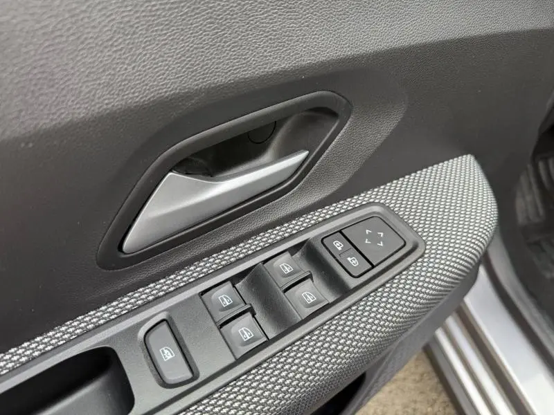 Gros plan sur la commande des vitres et la poignée intérieure côté conducteur du Dacia Jogger gris 2025.