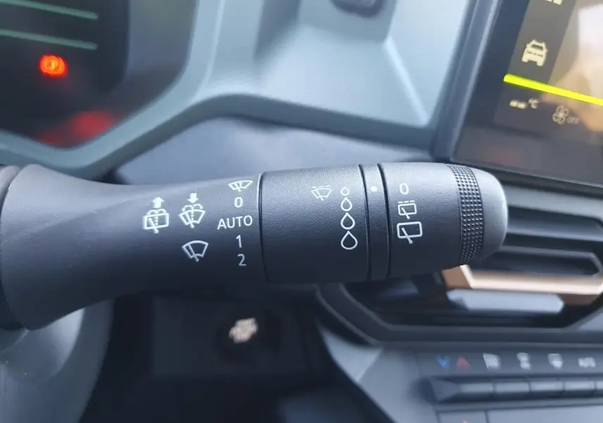 Gros plan sur la commande d’essuie-glace du Dacia Duster gris schiste, avec tableau de bord et écran tactile en arrière-plan.