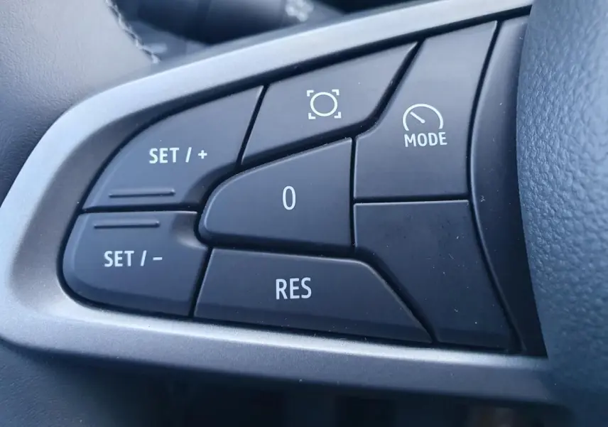 Gros plan sur les commandes noires du volant du Dacia Duster 2026, avec boutons de régulateur de vitesse et mode.