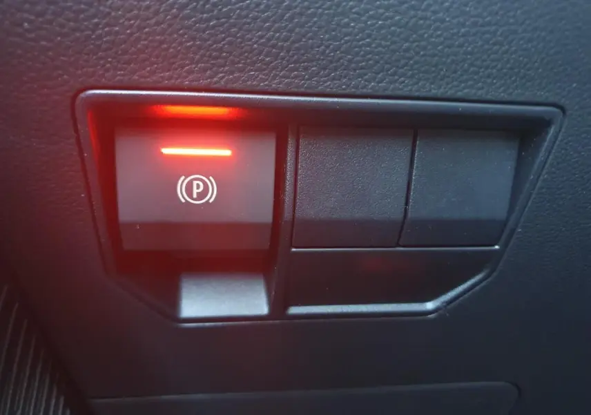 Gros plan sur le bouton de frein de stationnement électronique illuminé en rouge dans l'habitacle du Dacia Duster gris schiste.