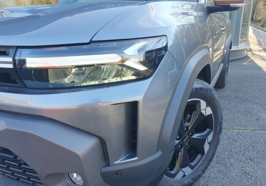 Gros plan sur l'avant droit du Dacia Duster gris schiste, mettant en valeur le phare LED et la jante alliage 17 pouces.
