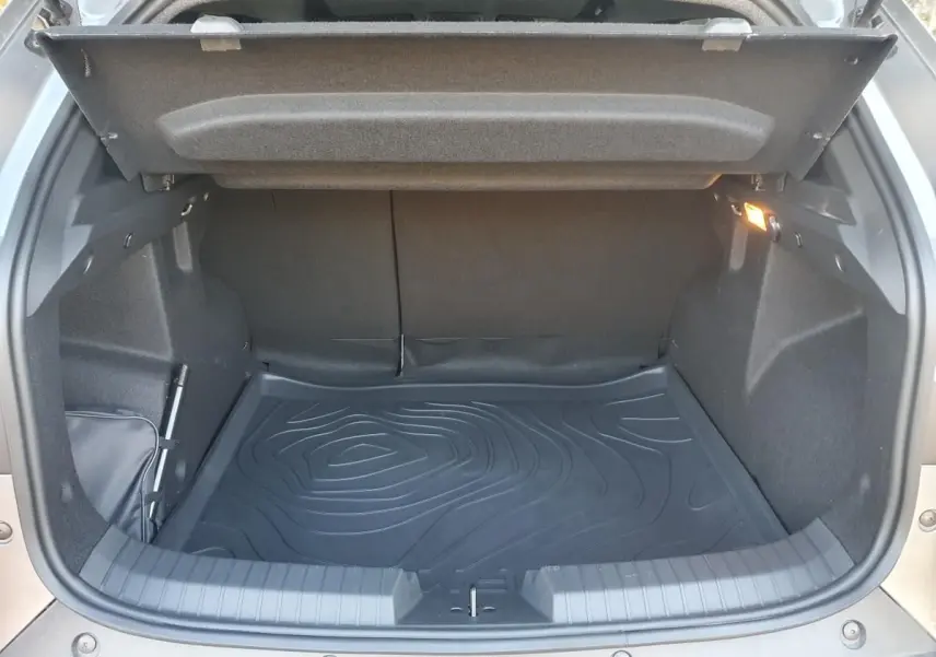 Coffre ouvert vu de l'arrière du Dacia Duster gris schiste, avec tapis de sol noir et éclairage intérieur allumé.