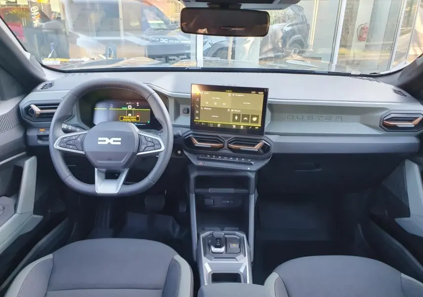 Vue intérieure frontale du tableau de bord du Dacia Duster 2026, avec écran tactile central et volant multifonction.