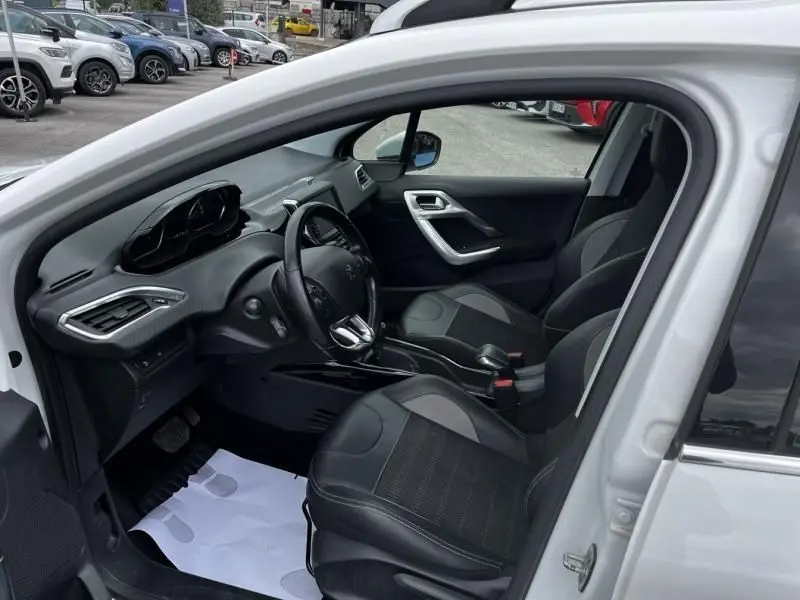 Intérieur de la Peugeot 2008 blanc vue côté conducteur, montrant le tableau de bord et les sièges noirs en tissu et cuir.