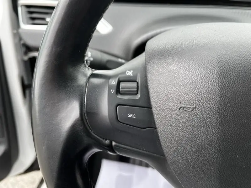 Gros plan sur le volant noir du Peugeot 2008 blanc de 2019, montrant les commandes audio côté gauche.
