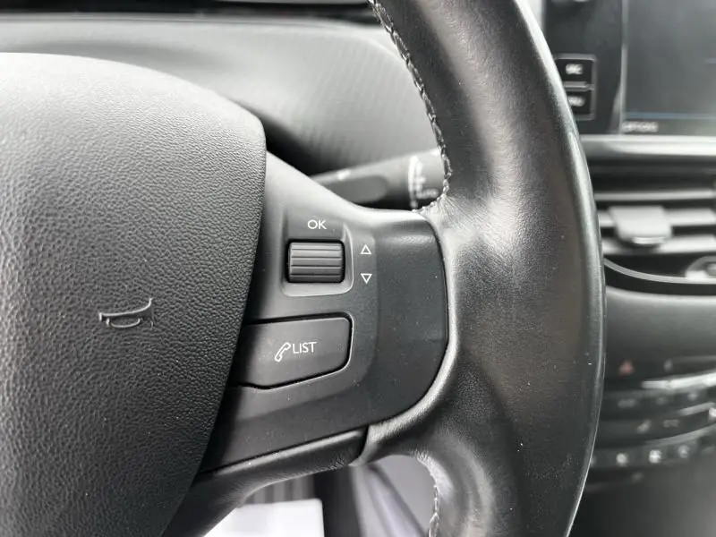 Gros plan sur la partie gauche du volant noir du Peugeot 2008 blanc 2019, avec commandes intégrées et tableau de bord en arrière-plan flou.