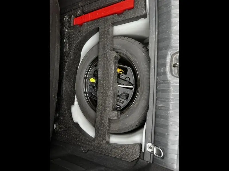 Roue de secours et outils de bord rangés dans le coffre d'une Peugeot 2008 blanche, vue plongeante sur le compartiment.