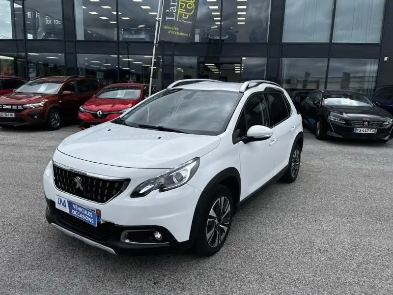Peugeot 2008 blanc vue 3/4 avant droit, avec toit ouvrant et jantes alliage, stationné devant un showroom.