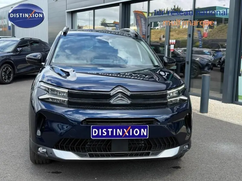 Vue avant d'un Citroën C5 Aircross 2025 bleu foncé avec calandre distinctive et logo chromé, devant un showroom.