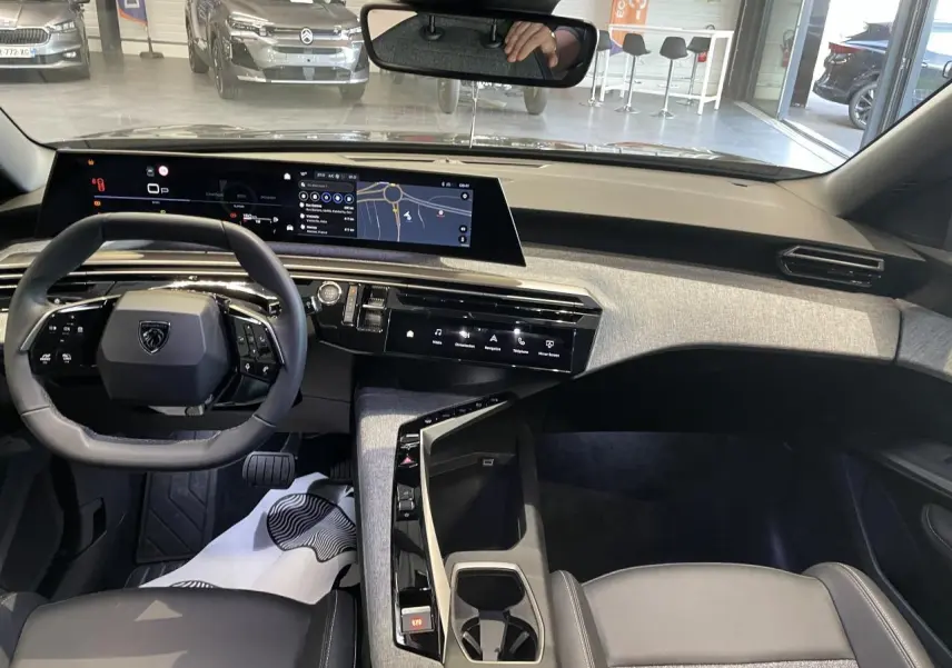 Vue intérieure du tableau de bord du Peugeot 3008 gris foncé 2025 avec écran incurvé et volant compact noir.