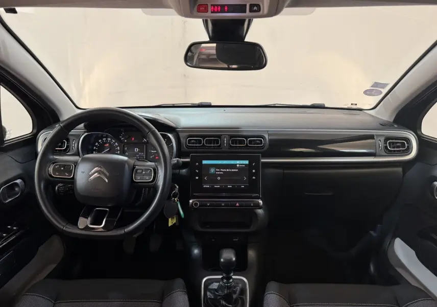 Vue frontale de l'intérieur noir du tableau de bord et volant cuir d'une Citroën C3 Shine Business 2019.