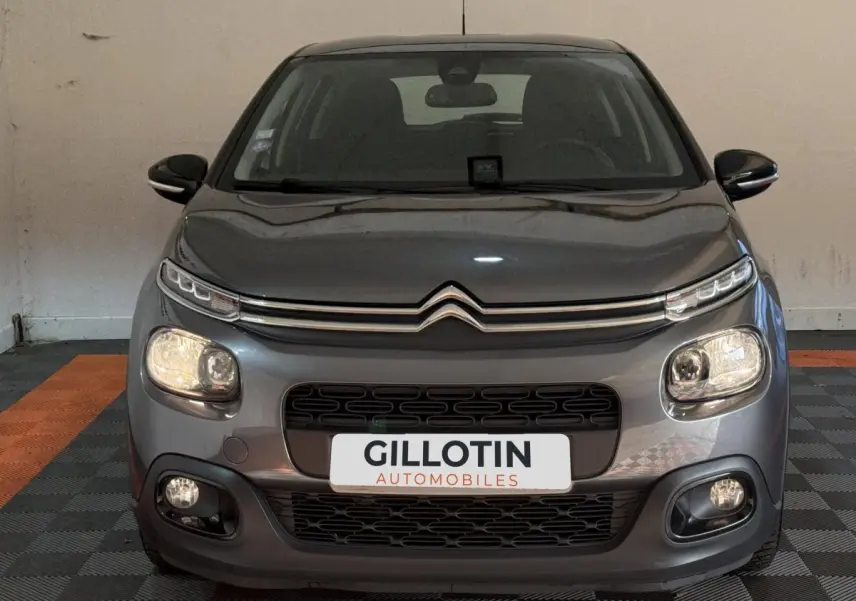 Vue frontale d'une Citroën C3 gris clair, avec phares allumés et calandre noire distinctive.