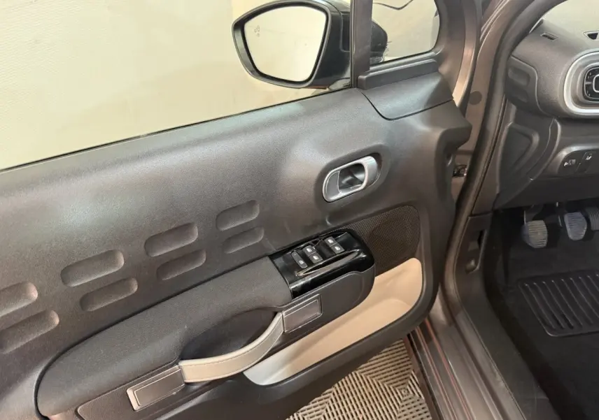 Vue intérieure côté conducteur de la porte noire et beige de la Citroën C3 gris clair avec commandes des vitres et rétroviseur.