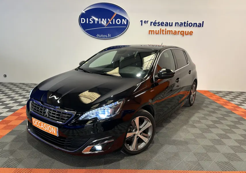 Peugeot 308 noire vue 3/4 avant droit avec phares allumés et jantes alliage dans showroom.