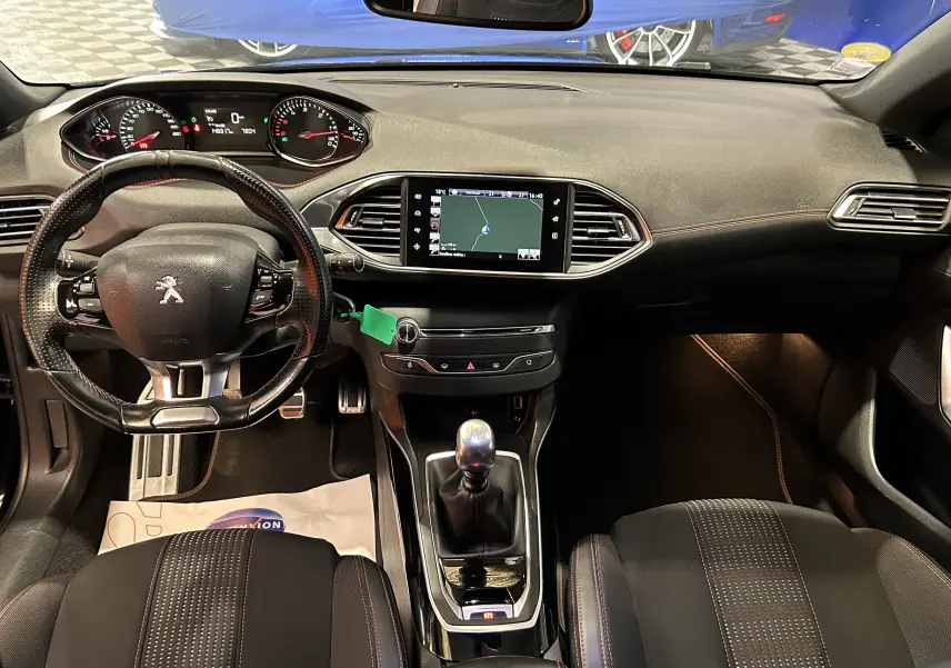 Vue intérieure avant de la Peugeot 308 noire, montrant le volant cuir, la console centrale avec GPS et la boîte manuelle.