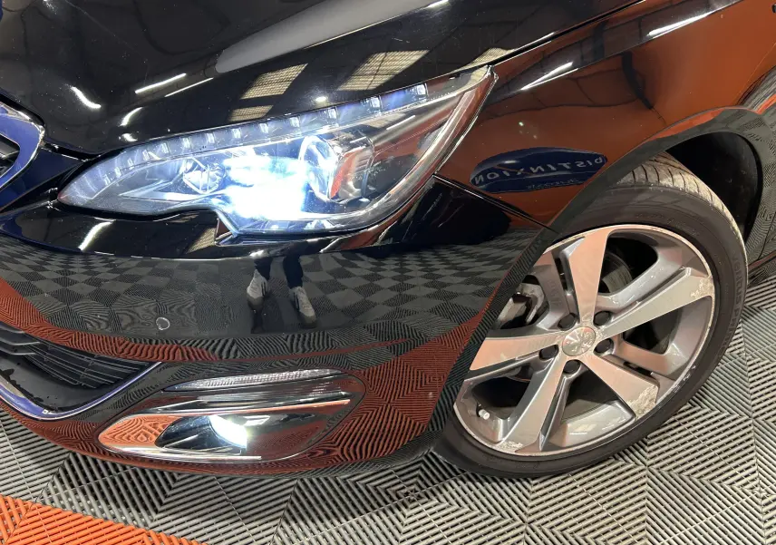 Gros plan sur l’avant droit noir d’une Peugeot 308 1.6 BlueHDi 120ch GT Line avec phares et antibrouillard allumés.