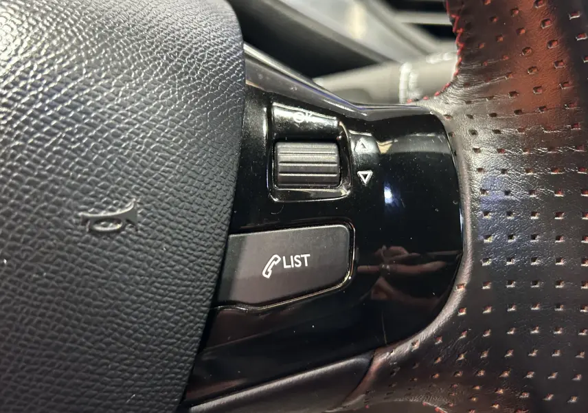 Gros plan sur les commandes noires du volant en cuir perforé avec surpiqûres rouges d'une Peugeot 308 GT Line 2017.