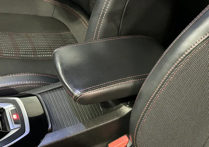 Gros plan intérieur sur l'accoudoir en cuir noir avec surpiqûres rouges entre les sièges avant d'une Peugeot 308 noire.