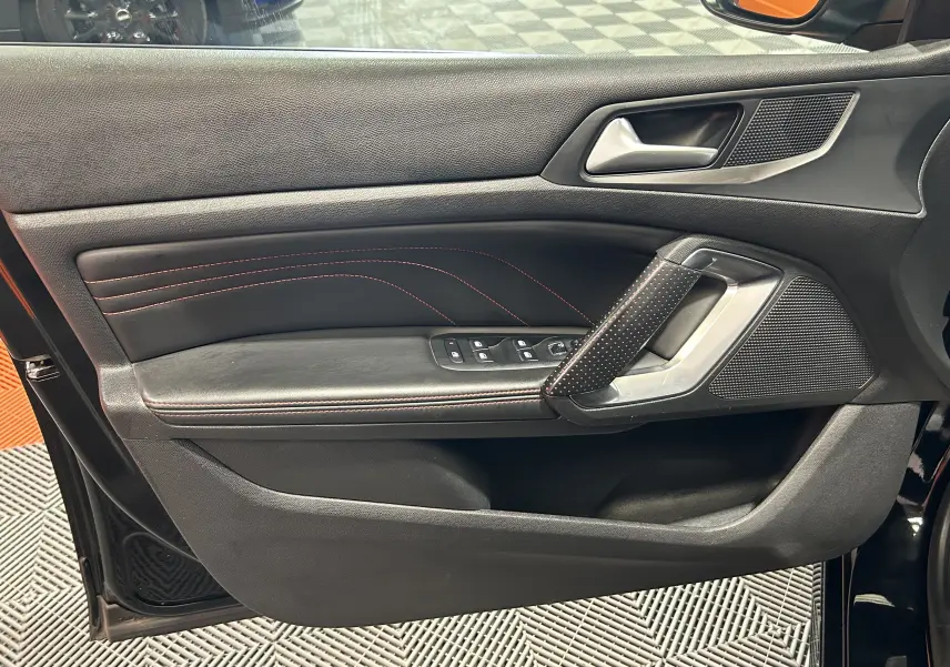 Vue intérieure côté gauche de la porte avant noire de la Peugeot 308 GT Line avec surpiqûres rouges et commandes électriques.