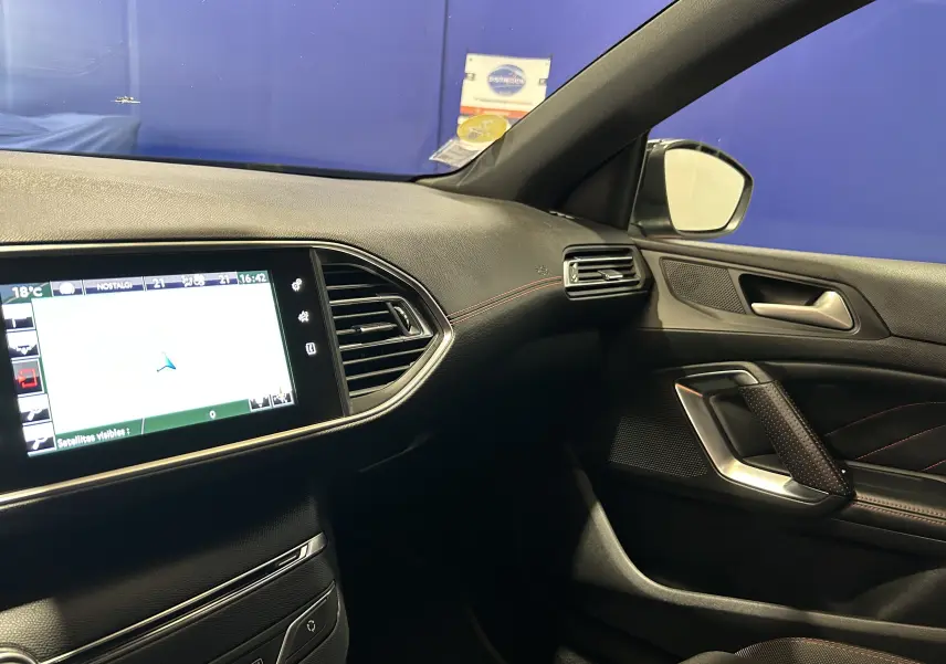 Vue intérieure côté passager de la Peugeot 308 noire, avec écran GPS tactile et finitions en cuir noir et surpiqûres rouges.