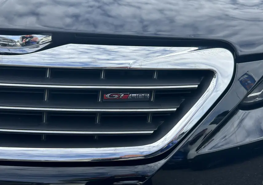 Gros plan sur la calandre chromée noire d'une Peugeot 308 GT Line avec logo distinctif rouge et noir.