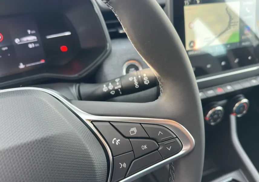 Gros plan sur le volant cuir multifonctions de la Renault Clio gris schiste avec commandes au volant et tableau de bord numérique.