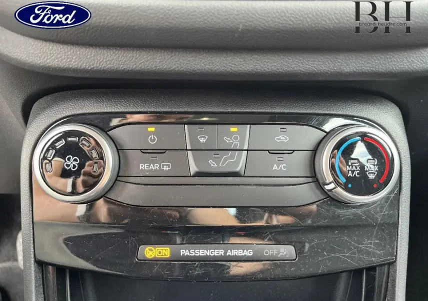 Gros plan sur la console de climatisation d’une Ford Puma bleu, avec commandes circulaires et affichage airbag passager.