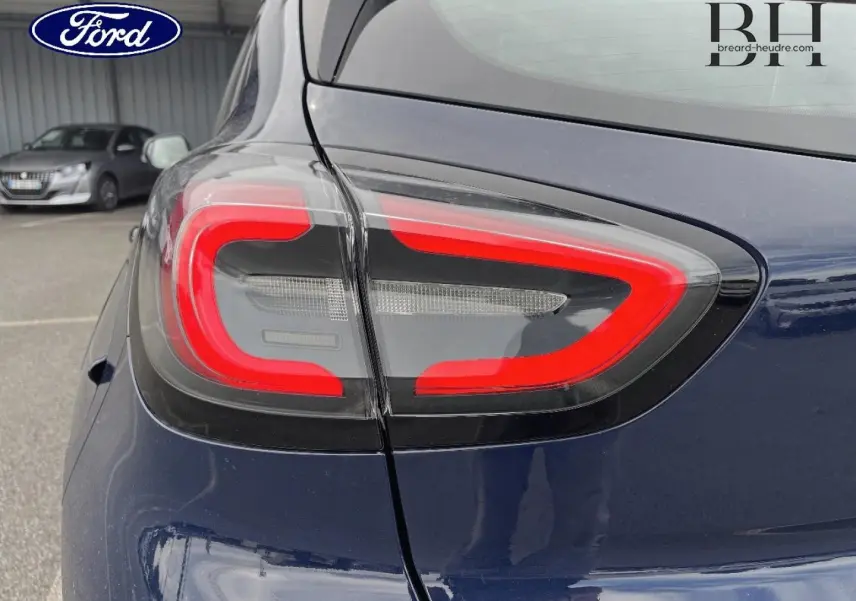 Gros plan sur le feu arrière gauche rouge et noir du Ford Puma bleu Abysse 2023, avec reflet du ciel et arrière-plan flou.