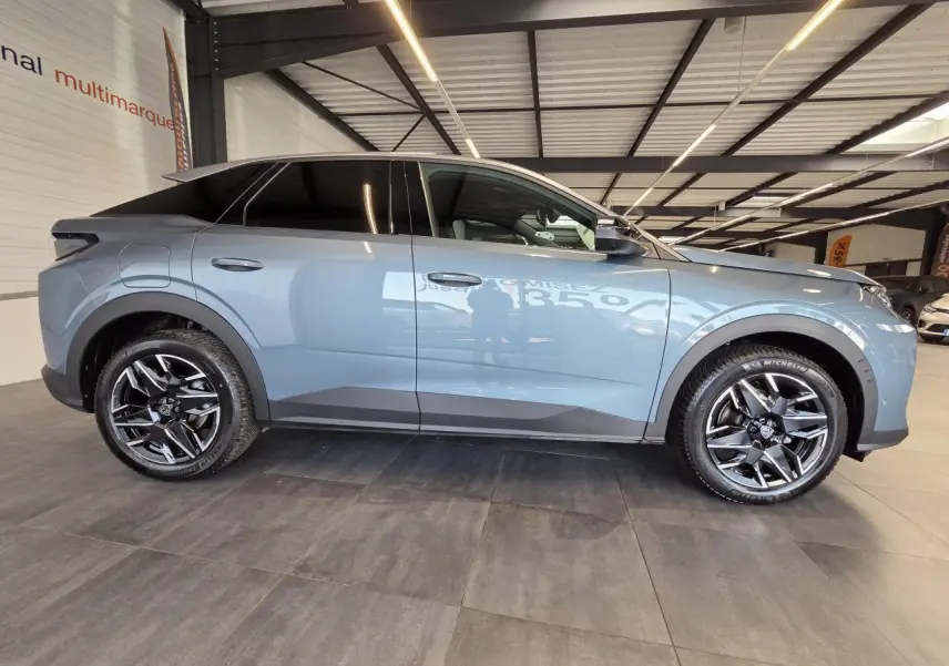 Vue de profil côté gauche du Peugeot 3008 hybride 2025 bleu clair avec jantes alliage 19'' noir brillant en intérieur showroom.