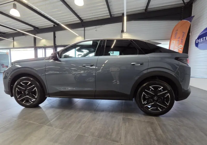 Vue latérale droite d’un Peugeot 3008 hybride 2025 gris métallisé avec jantes alliage noires et toit noir brillant en intérieur showroom.