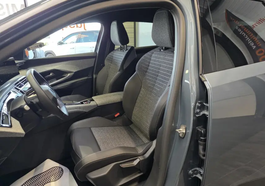 Vue intérieure côté conducteur du Peugeot 3008 2025 bleu clair, avec sièges tissu et cuir bicolore gris et noir.
