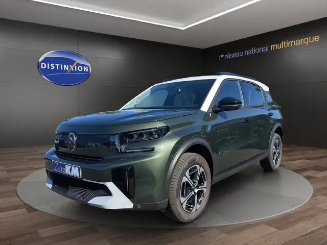 Vue 3/4 avant d'un Citroën C3 Aircross hybride vert avec toit blanc et jantes modernes en showroom.