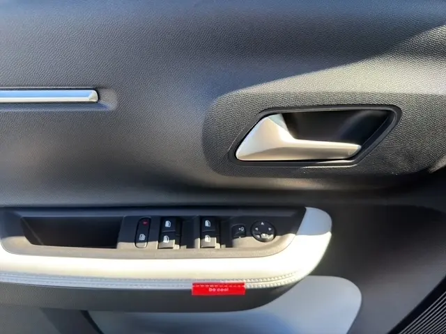 Gros plan sur la poignée intérieure et les commandes de vitres de la porte avant gauche d'une Citroën C3 Aircross hybride verte.