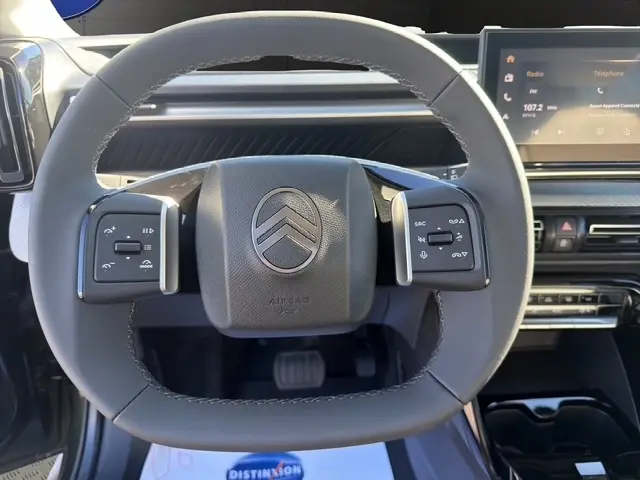 Vue rapprochée du volant cuir multifonctions gris du Citroën C3 Aircross hybride 2026 avec écran tactile en arrière-plan.