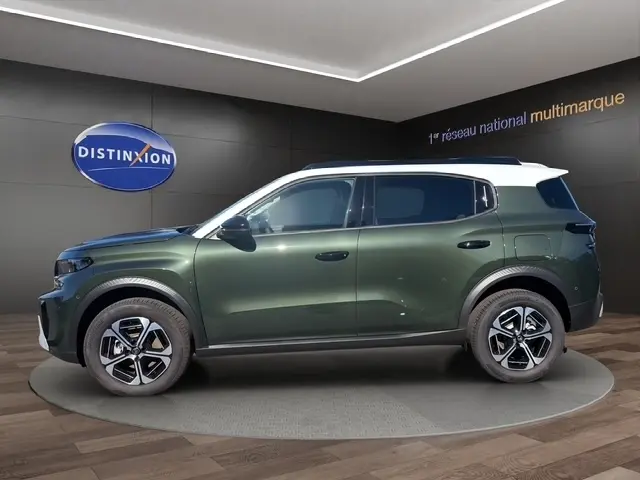 Vue latérale gauche d'un Citroën C3 Aircross hybride vert avec toit blanc et jantes distinctives en showroom.