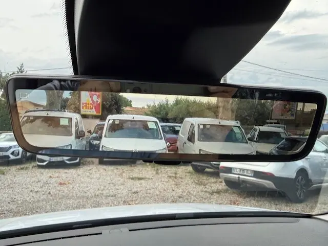Vue arrière dans le rétroviseur intérieur d’un Citroën Berlingo blanc 2026, version utilitaire diesel, stationné parmi d’autres véhicules.