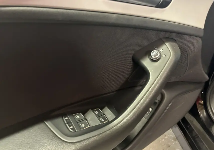 Gros plan sur la commande des vitres et rétroviseurs côté conducteur d'une Audi A6 Avant noire de 2017.