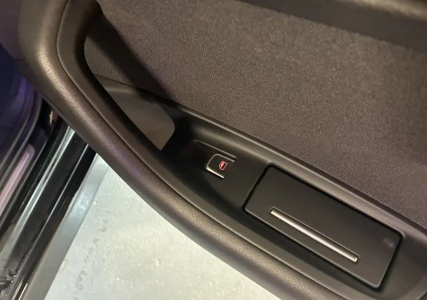 Gros plan sur la commande de lève-vitre côté gauche d'une Audi A6 Avant noire, finition tissu noir.