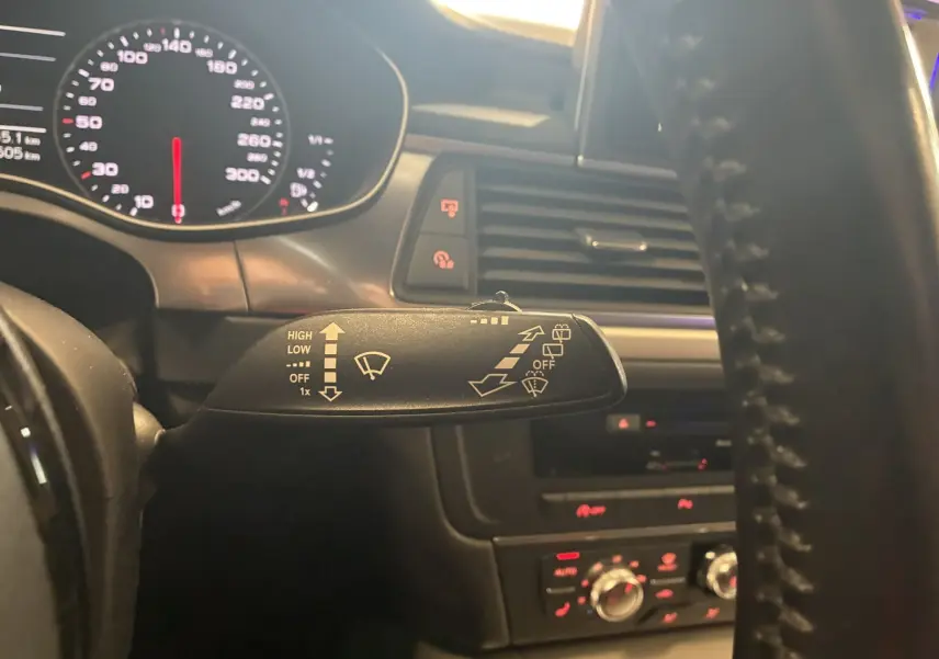 Gros plan sur la commande des essuie-glaces à gauche du volant dans l'habitacle noir d'une Audi A6 Avant 2017.