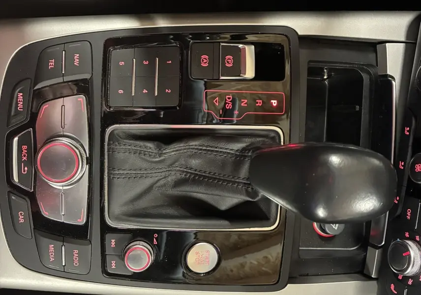 Vue rapprochée de la console centrale noire de l'Audi A6 Avant 2017, avec levier de vitesses automatique et commandes éclairées rouge.