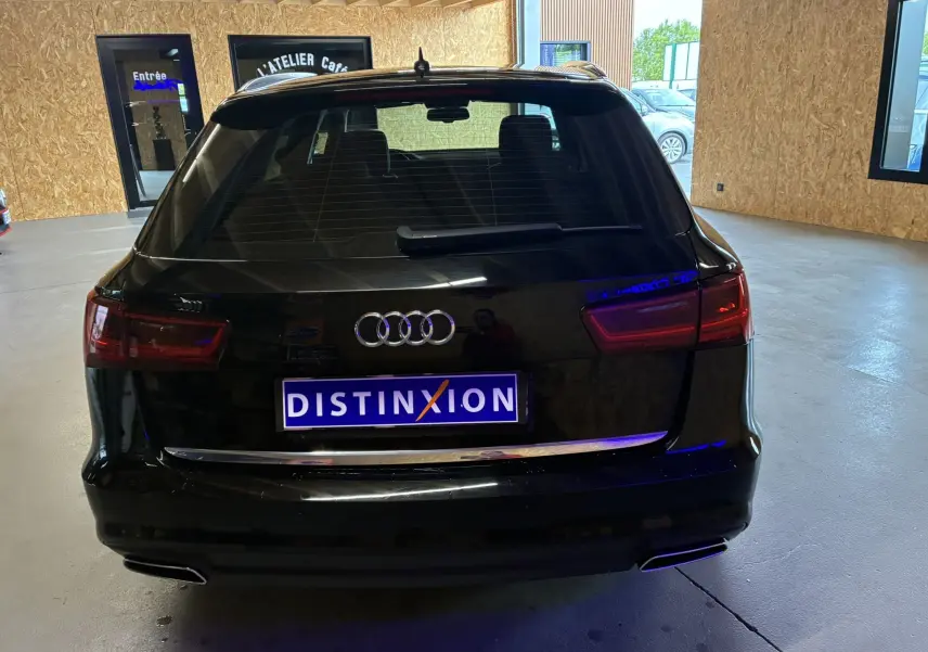 Vue arrière d'une Audi A6 Avant noire de 2017, avec feux arrière allumés et plaque Distinxion visible.