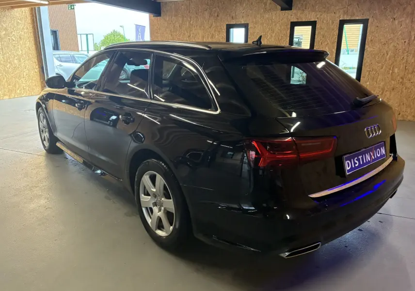 Audi A6 Avant noir vue 3/4 arrière droit en intérieur, avec feux arrière LED et jantes alliage cinq branches.