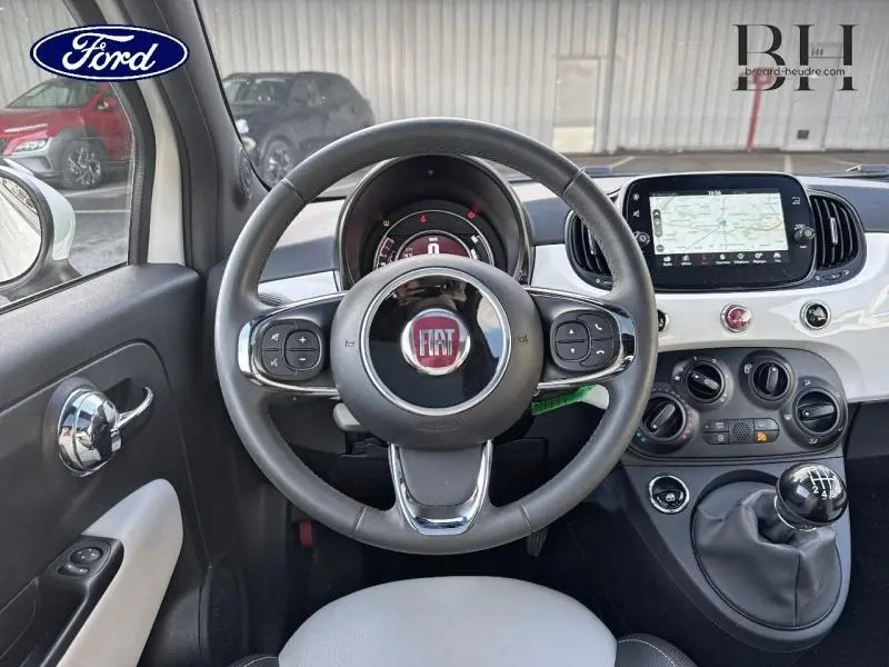 Intérieur de la Fiat 500 blanche vue du poste de conduite, volant cuir multifonction et écran tactile central.