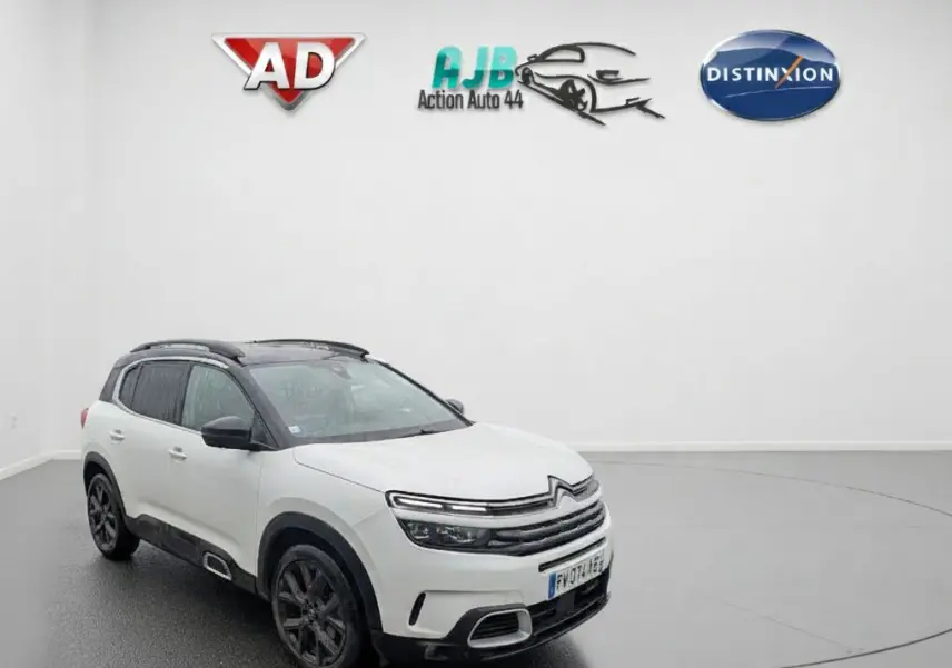 Vue 3/4 avant droite d'un Citroën C5 Aircross blanc nacré avec toit noir et jantes noires en intérieur showroom.