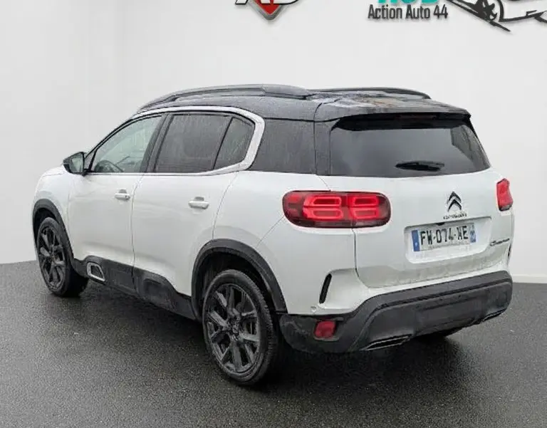 Vue 3/4 arrière droite d'un Citroën C5 Aircross blanc nacré avec toit noir et jantes foncées sur sol humide.
